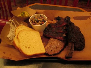 (clockwise): pork ribs, beef rib, and brisket with onions, pickles, Texas caviar, and white bread